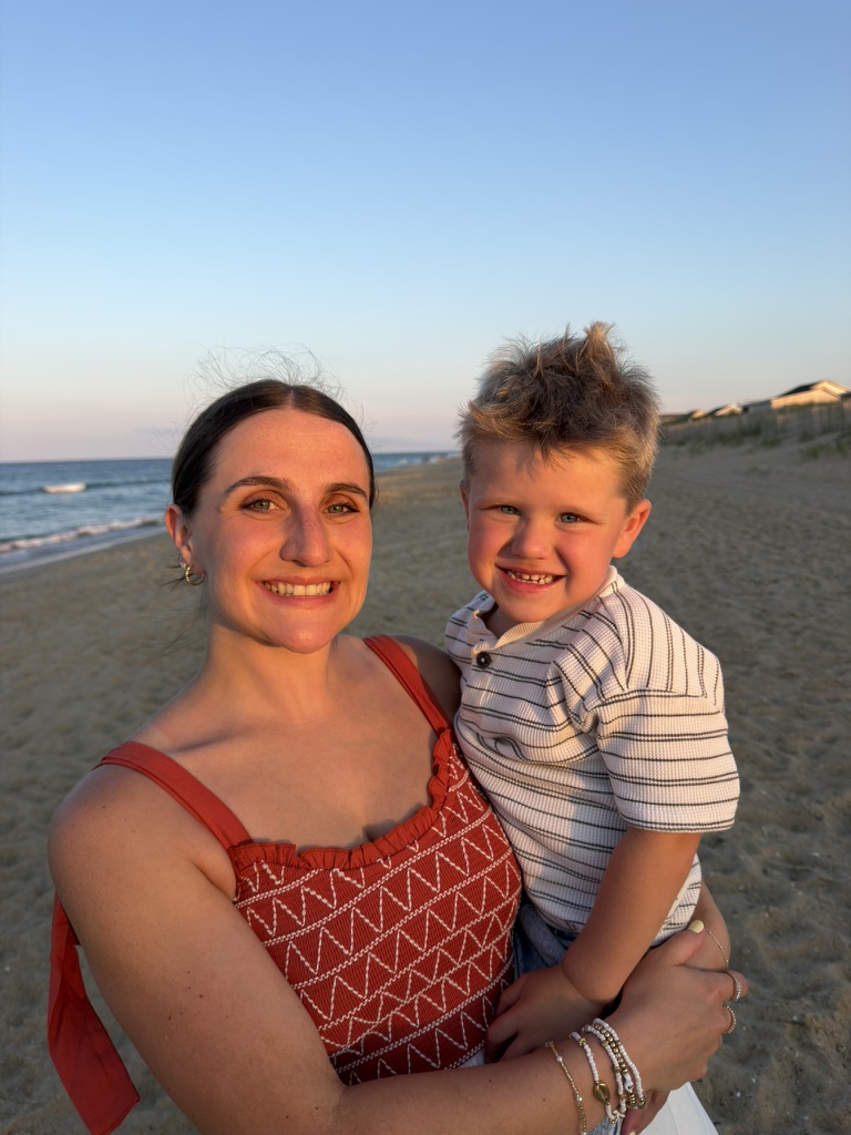 Rachel and a toddler smiling on the beach at sunset